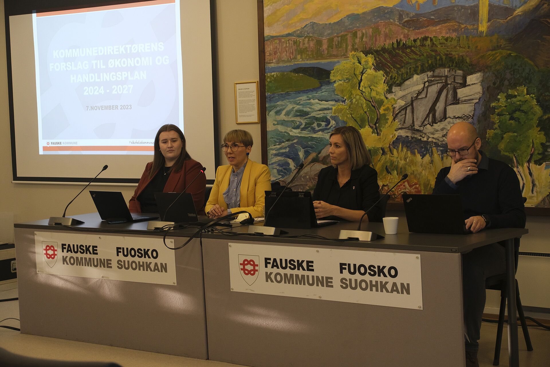 Fire personer som sitter bak et bord med mikrofoner og på skjerm bak vises framlegg av forslag til økonomi- og handlingsplan i Fauske kommune. Personene som er avbildet er: Ingrid Navjord, Ellen Beate Lundberg, May-Britt P. Delbekk og Mads Sandvik.
